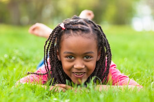 Outdoor portrait of a cute young black girl  lying down on the grass and smiling - African people