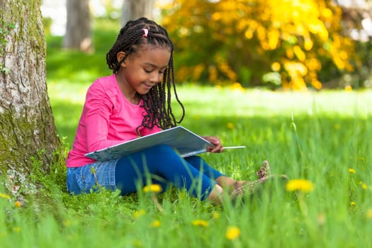Outdoor portrait of a cute young black little  girl reading a book - African people