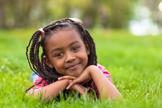 Outdoor portrait of a cute young black girl  lying down on the grass and smiling - African people