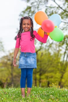 Outdoor portait of a cute young  little black girl playing with balloons - African people