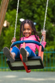 Outdoor  portrait of a cute young black girl playing with a swing - African people