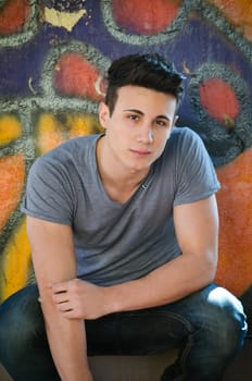 Attractive young man sitting outdoors in front of graffitti covered wall