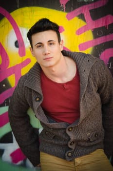 Attractive young man standing outdoors in front of graffitti covered wall