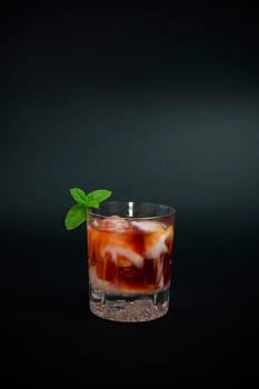 Cocktail made with red liquor, vodka and a few drops of white yogurt liquor decorated with mint leaves on dark background.