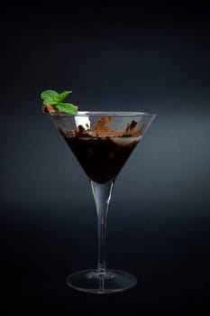 Cocktail made with chocolate liquor, coffe, banana liquor and guarnished with stick of cinnamon and mint leaves on dark background.