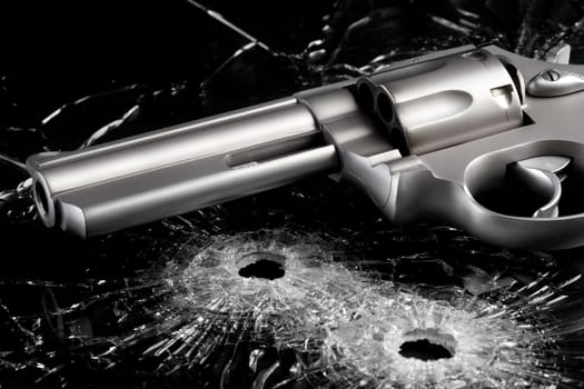 Gun with two bullet holes in glass over black - modern revolver close up