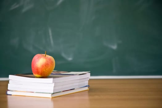 Books and apple with used green chalkboard and erasers in the background