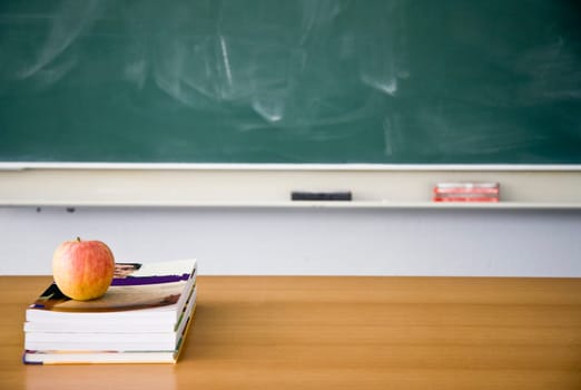 Books and apple with used green chalkboard and erasers in the background