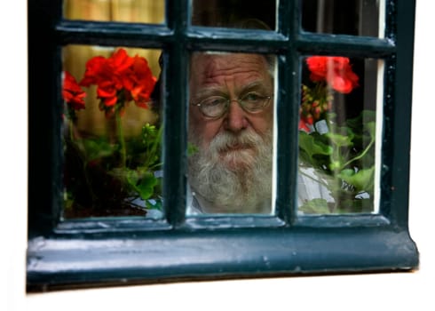Old man with grey beard looking through the window