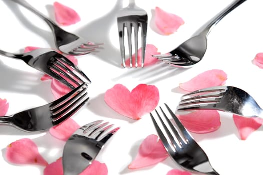 forks surrounding a heart shape petal with rose petals for a concept on romantic dining on white background
