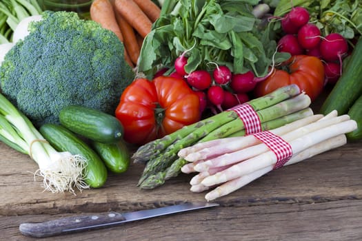 Fresh green and white asparagus lies on an old wooden board along with other spring vegetables and a knife
