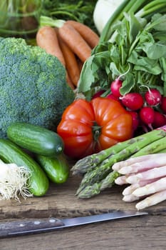 Fresh seasonal vegetables lie on an old wooden board together with a knife