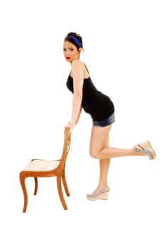 A young pretty woman in pin up style standing on a chair with shorts and high heels and a blue headband in her hair, for white background.