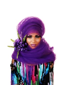 A young woman sitting for white background with purple twill around her head and long eye lashes, looking into the camera.