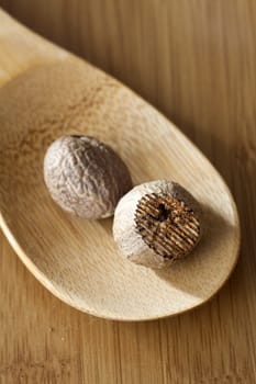 Two nutmegs on a wooden spoon on a wooden surface