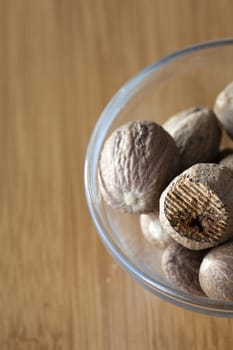 View from above to a glass bowl with some whole and a rubbed nutmeg