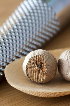 Two nutmegs on a wooden spoon and in the background a musca drive out of focus