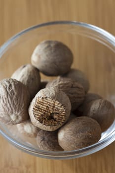 View from above to a glass bowl with some whole and a rubbed nutmeg