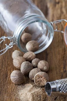 Nutmegs lie in front of and in a spice jar on a rustic wooden surface