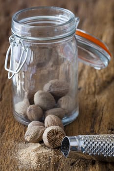 Nutmeg in the spice jar in front of it lies a musca shoot on a rustic wooden surface