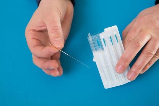 Acupuncture needles in doctor hands holding blister on blue
