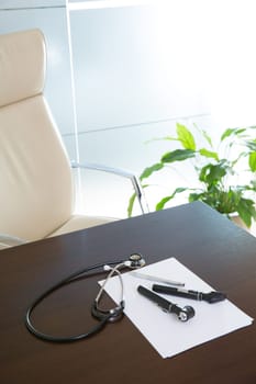 Doctor office table desk and beige chair with stethoscope otoscope and white paper