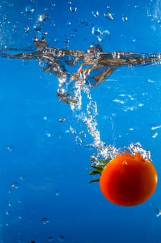 red tomato dropped into the water with blue background