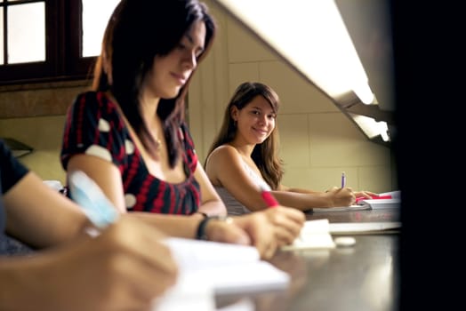 Portrait of happy female student writing and preparing test, pretty girl smiling at camera in college library