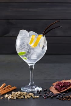 Gin tonic cocktail with ice vanilla lima and varied spices on black background