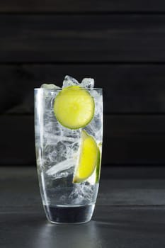 Gin tonic cocktail with lima and ice cube on black slate stone background