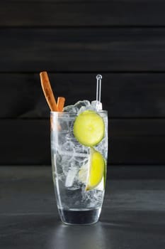 Gin tonic cocktail with lima cinnamon and ice cube on black background