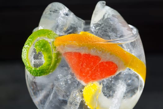 Gin tonic cocktail macro with lima lemon and grapefruit closeup detail on black