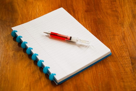 Scribbling-block and ball-point like a syringe needle on wooden table