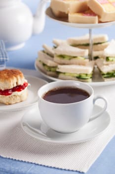 Afternoon cup of tea with cucumber sandwiches and scones in the background.