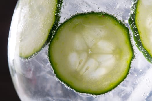 Gin tonic cocktail with cucumber and ice  macro closeup on black