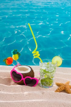 Mojito cocktail on beach sand with coconut and sunglasses in summer vacation