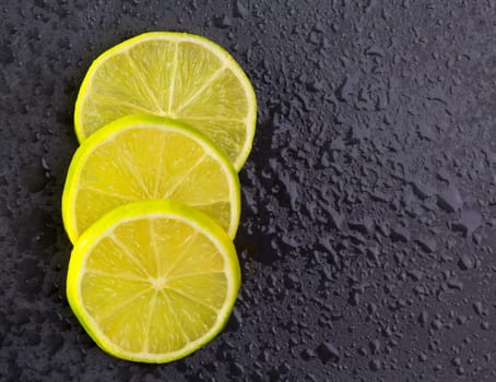 Fresh lima slices with water drops on black slate stone background