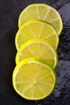 Fresh lima slices with water drops on black slate stone background