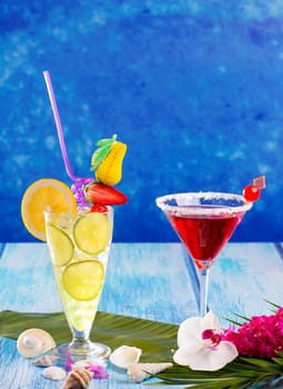Lemon Mojito and red Margarita cocktails in Caribbean blue wood with flowers and seashells