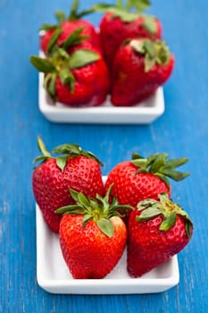 Closeup of large fresh strawberries in two white dishes on light blue wooden background