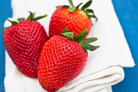 Closeup of three large fresh strawberries resting on white cloth against light blue wooden background