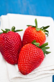 Closeup of three large fresh strawberries resting on white cloth against light blue wooden background