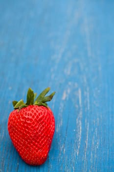 Closeup of one large fresh strawberry against light blue wooden background