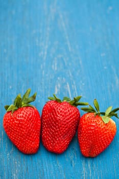 Closeup of three large fresh strawberries in row against light blue wooden background