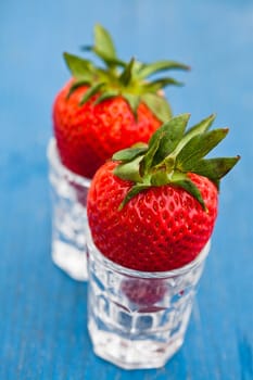 Closeup of two large fresh strawberries resting in small glasses against light blue wooden background