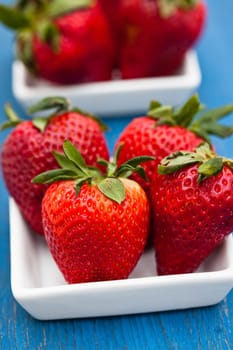 Closeup of large fresh strawberries in two white dishes on light blue wooden background