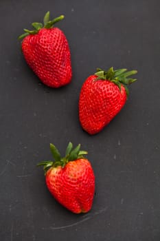 Closeup of three large fresh strawberries against dark background
