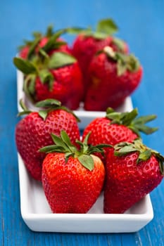 Closeup of large fresh strawberries in two white dishes on light blue wooden background