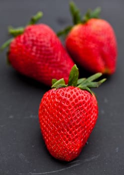 Closeup of three large fresh strawberries against dark background