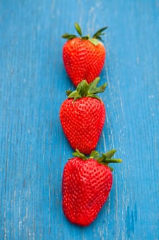 Closeup of three large fresh strawberries in row against light blue wooden background